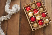 Christmas ornaments background with colorful gold and red baubles in a box alongside a silver tinsel border with copyspace for your greeting on a wooden background, overhead view