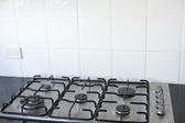 Clean modern gas stove with five burners in a black kitchen counter with white splash back