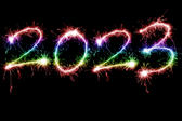 rainbow coloured sparkling fireworks as happy new year holiday 2023 over black background