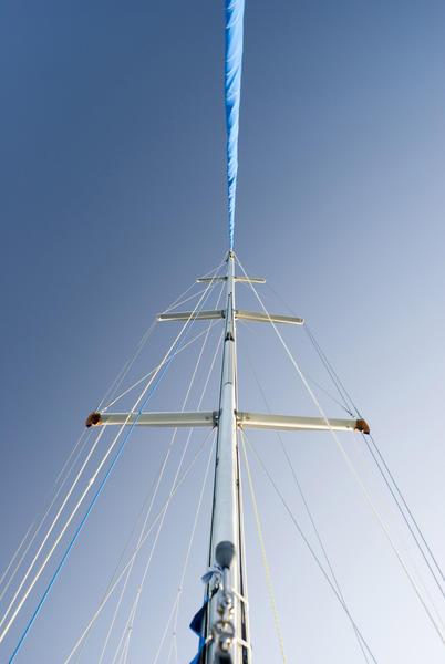Metal mast of a small pleasure sailing yacht with its rigging against a clear blue sky