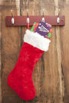 Colorful red Christmas stocking filled with small gifts hanging from a metal hanger on a wooden wall with copyspace