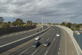 Cars travelling towards the camera on a multi lane highway which curves away to the left under a cloudy sky