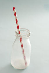 Empty used glass milk bottle with a striped straw and the remnants of the drink in the bottom over a grey background with copy space